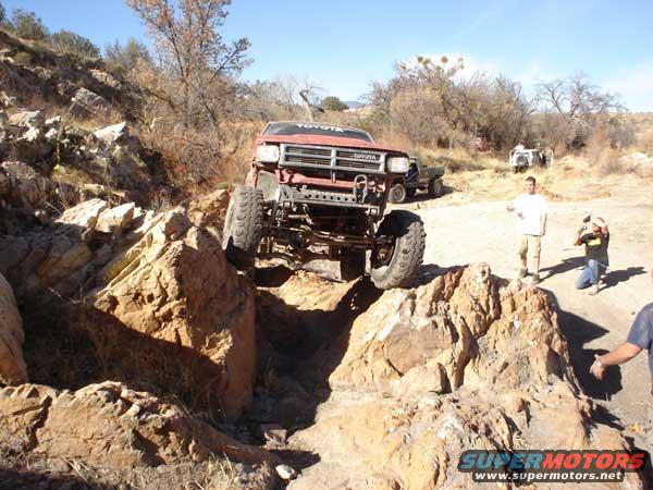 Red Toyota truck climbing rocks, front 3/4 view. Readable text on grille