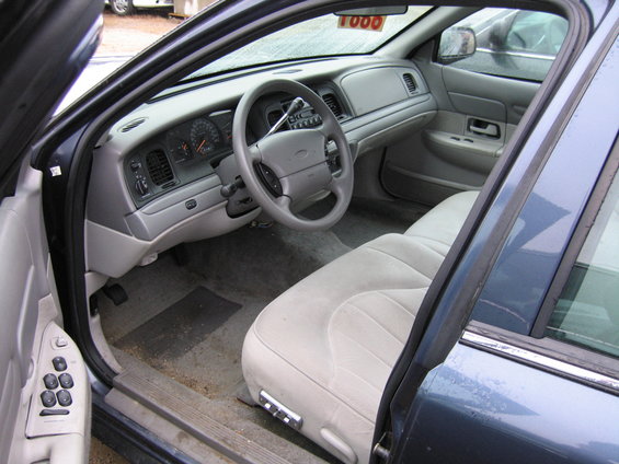 1991 Ford Crown Victoria LTD interior, tan seats, gray dashboard, visible odometer and steering wheel. A red 'TOOD' tag hangs from the rearview mirror