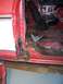 1978 Ford Bronco - The lower door post and floor of a red vehicle show significant rust damage, with a black seat in the background.