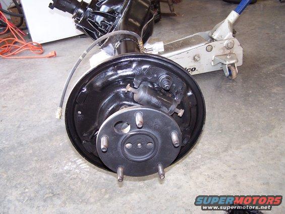 Rear axle assembly with drum brake, black, on concrete floor with a floor jack