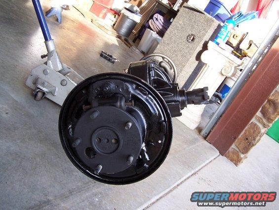 Rear axle assembly with drum brake and brake shoes, resting on a concrete floor next to a floor jack