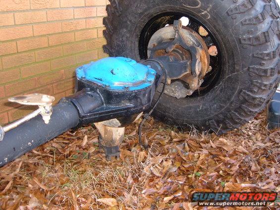 Axle assembly with blue differential cover and large tire, resting on dry leaves