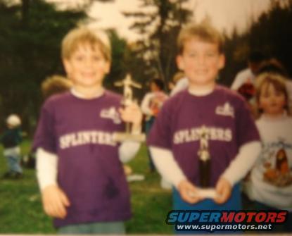 Two young boys in purple 'Splinters' t-shirts hold trophies outdoors