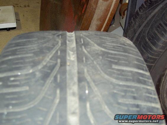 Close-up of a tire's tread pattern. Text at bottom reads SUPERMOTORS.NET
