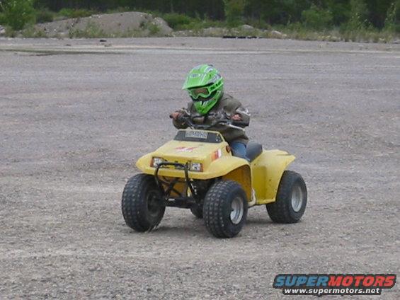 Yellow ATV with a child wearing a green helmet riding on gravel