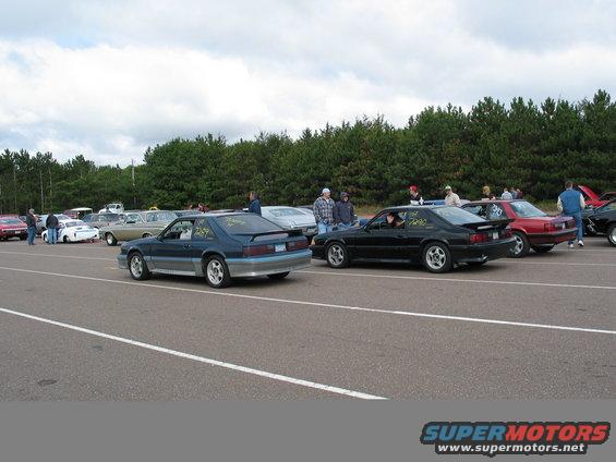 Blue and black 1990 Ford Mustangs on a racetrack, side-by-side