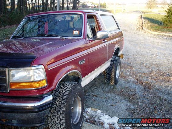Maroon 1993 Ford Bronco with lifted suspension and large tires parked on a gravel road