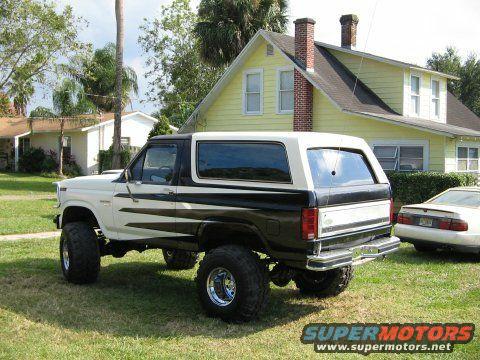 White and black lifted Ford Bronco with aftermarket wheels parked on grass