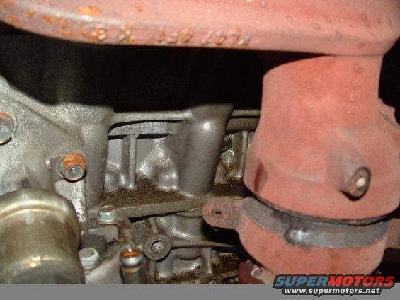 Engine block with exhaust manifold, showing metal casting and bolts. Text 'KL47 4FC K 8' is visible on a pipe