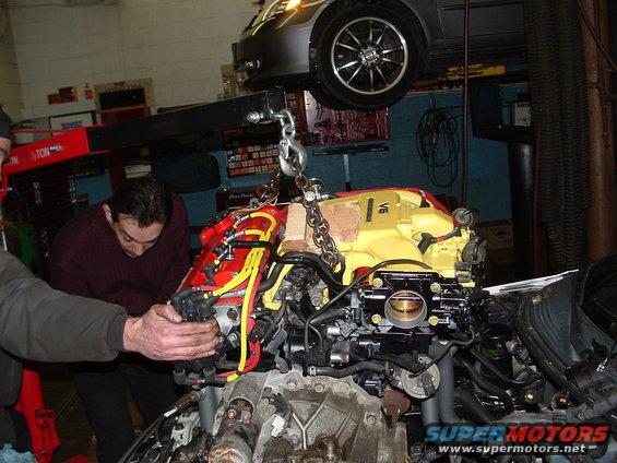 Engine being lifted by a chain hoist in a garage with mechanics working on it