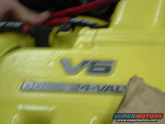 Yellow engine valve cover with V6 and 24-VAL emblems. A hand is visible near red spark plug wires