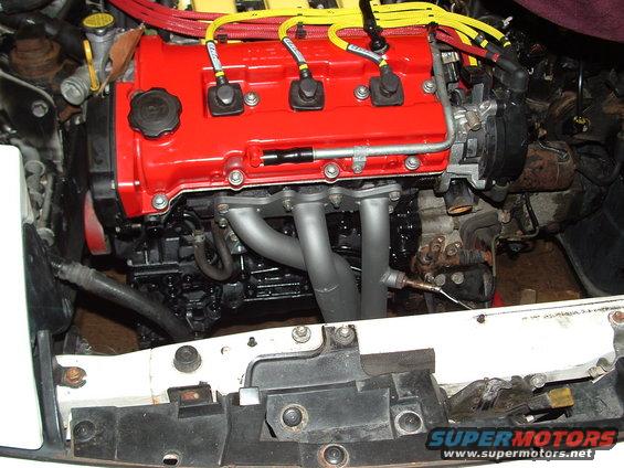 Engine with red valve cover and silver exhaust manifold, wires visible