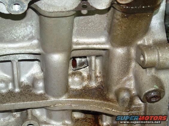 Close-up of a dirty engine block with some oil residue. Shows a small metal protrusion in a recessed area