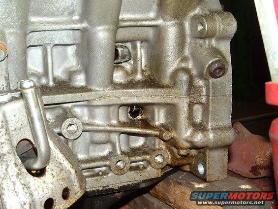 Close-up of a dirty, cast-metal engine block section with various bolt holes and a small crack