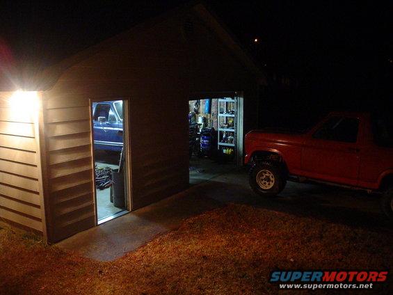 Red pickup truck parked outside garage, blue pickup truck inside garage
