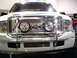 1986 Ford Bronco - Frontal view of a white Ford truck a prominent chrome grille and a bull bar with auxiliary lights.
