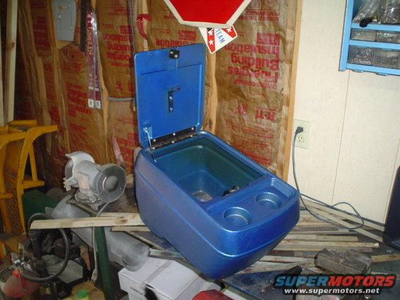 Blue plastic center console with open lid and two cup holders, sitting on a workbench