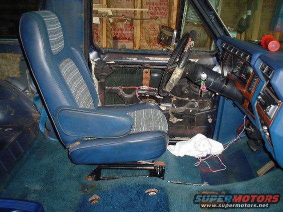 Blue fabric and vinyl interior seat with armrest, dashboard with wood trim, and steering wheel