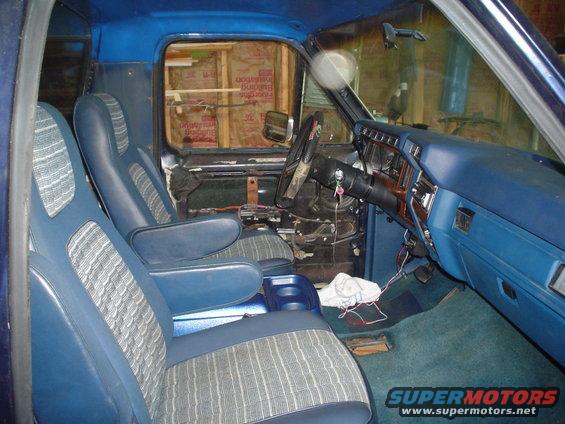Interior view of a blue truck's front seats, dashboard, and steering wheel. Door panel is removed