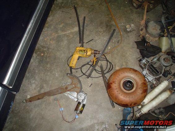 Yellow drill, torque converter, window regulator, and other car parts on concrete floor