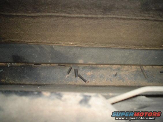 Close-up of the underside of a vehicle, showing some metal framing and what appear to be cut wires or tubes