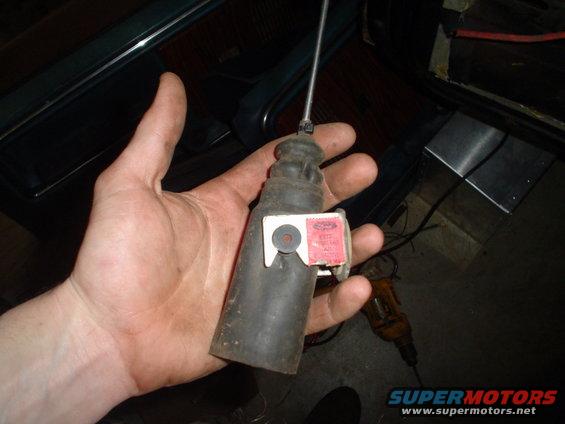 Hand holding a black car part with a red Ford label attached