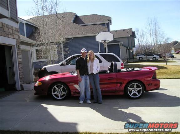 Red convertible sports car with a white SUV behind it, two people standing beside the car