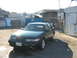 1995 Ford Taurus - A dark green sedan is parked in an industrial area with a chain-link fence and buildings in the background.