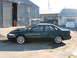 1995 Ford Taurus - A dark green 1995 Ford Taurus SHO sedan is parked outside a corrugated metal building, its side profile and aftermarket wheels.