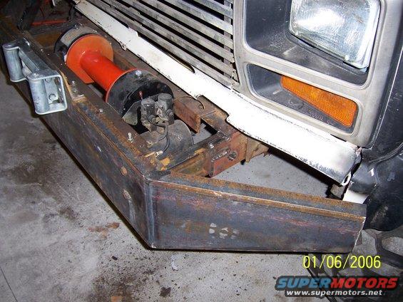 Custom steel bumper with a red and black winch mounted. Part of a vehicle grille and headlight visible above