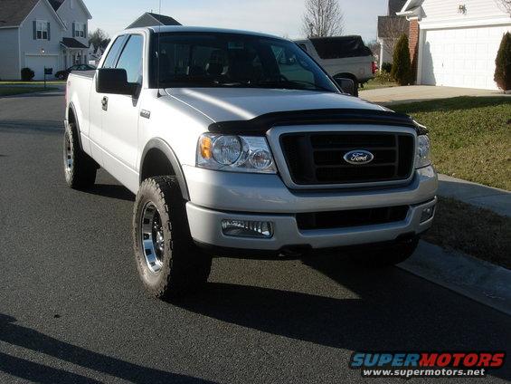 Silver Ford F-150 pickup truck with aftermarket wheels and tires, parked on a residential street
