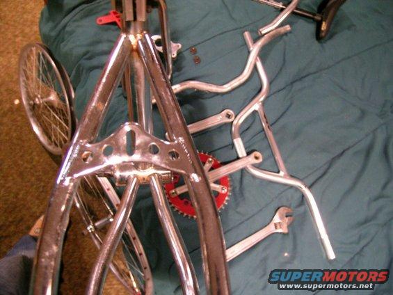 Chrome bicycle frame with red sprocket and handlebars laid out on a teal cloth