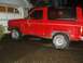 1985 Ford Bronco II - A red 1985 Ford Bronco II is parked on a wet driveway next to a garage.