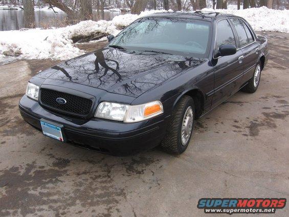 Dark blue 2003 Ford Crown Victoria, front 3/4 view, parked on concrete with snow in background