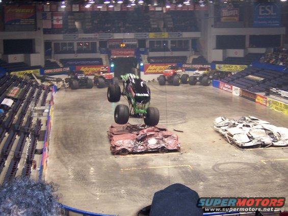 Monster truck in mid-air over crushed cars at an indoor event