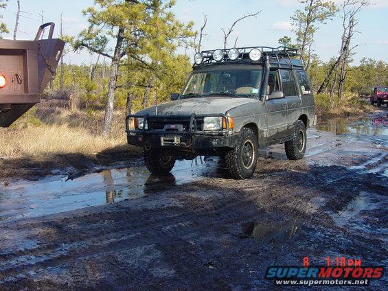 Off-road SUV with roof rack and lights driving through mud and puddles