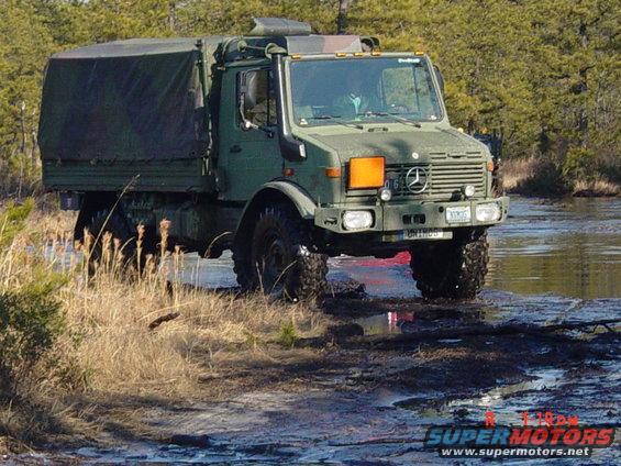 Green Mercedes-Benz Unimog truck driving through muddy water