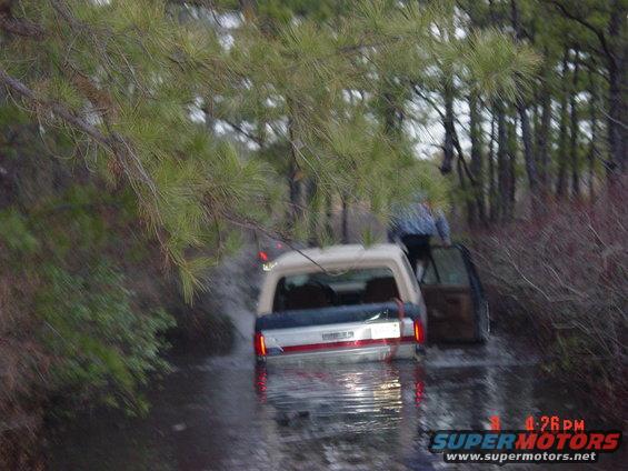 Rear view of a 1995 Dodge 1500 stuck in water, with a person exiting the passenger side