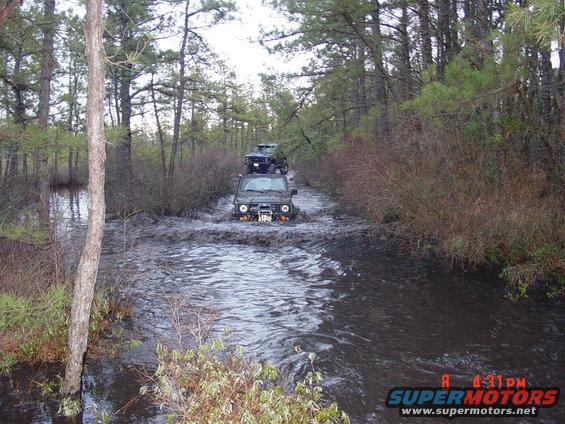 Two off-road vehicles driving through a flooded wooded area