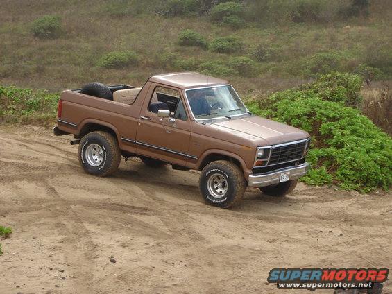 Brown 1985 Ford Bronco on dirt road with spare tire in the back