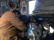 1978 Ford Bronco - Mechanics are installing a new engine into a vehicle in a garage setting.