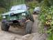 1990 Ford Bronco - Modified SUV with significant damage to the front end is attempting to climb over rocks.