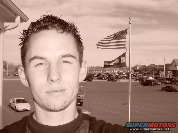 Man in foreground, American and Colorado flags, parking lot with cars
