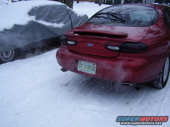 Red sedan with a spoiler and tinted taillights parked in the snow next to a car covered with a tarp