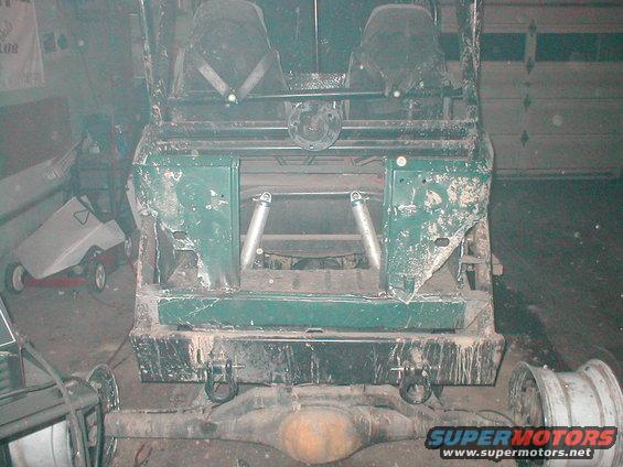 Rear frame and suspension of a green vehicle, possibly a Bronco, with two seats visible. The body is damaged
