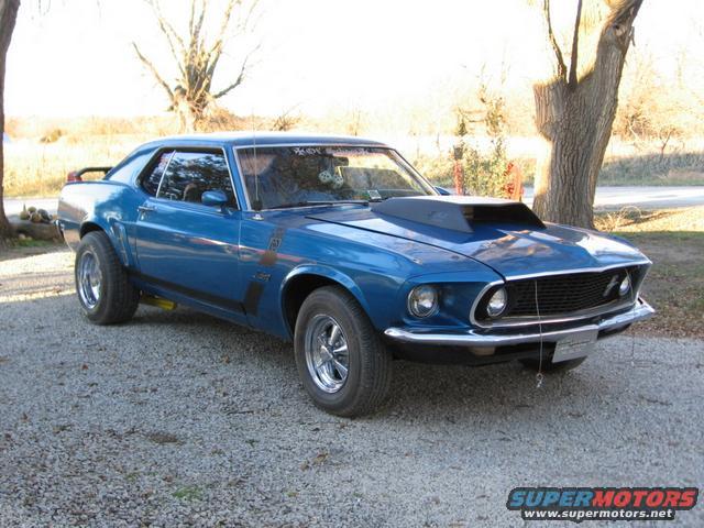 Blue 1969 Ford Mustang Boss 302 with a hood scoop parked on gravel