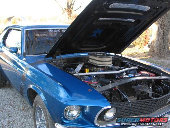Blue 1969 Ford Mustang with hood open showing engine. Has a chrome air cleaner and racing stripes on the fender
