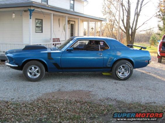 Blue 1970 Ford Mustang Boss 302 with black stripes and a hood scoop parked in front of a house