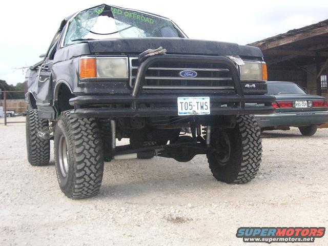 1990 Ford Bronco with lifted suspension, off-road tires, and damaged windshield. Another car is parked behind it
