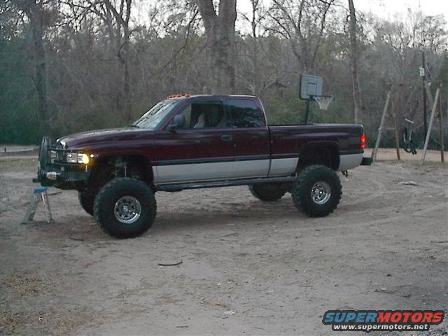 Maroon and silver lifted 2001 Dodge 1500 pickup truck with large off-road tires parked on dirt